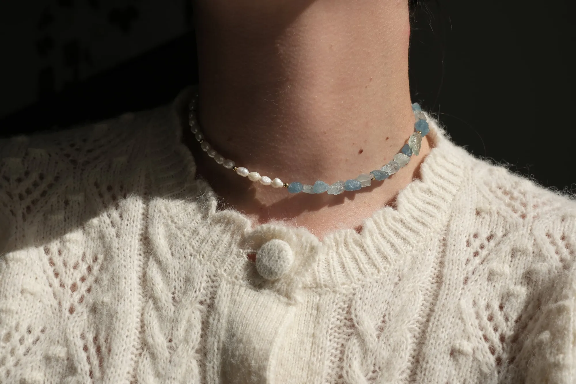 The Acvamarin necklace worn over a cream knit — raw aquamarine and freshwater pearls